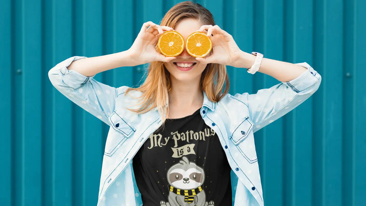 Smiling woman holding orange slices over her eyes while wearing a funny sloth T-shirt with a playful expression