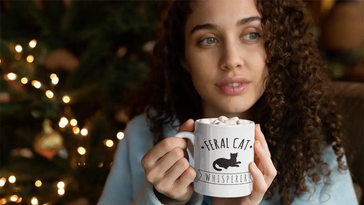 Woman holding a white feral cat mug with marshmallows in a cozy holiday setting near Christmas tree