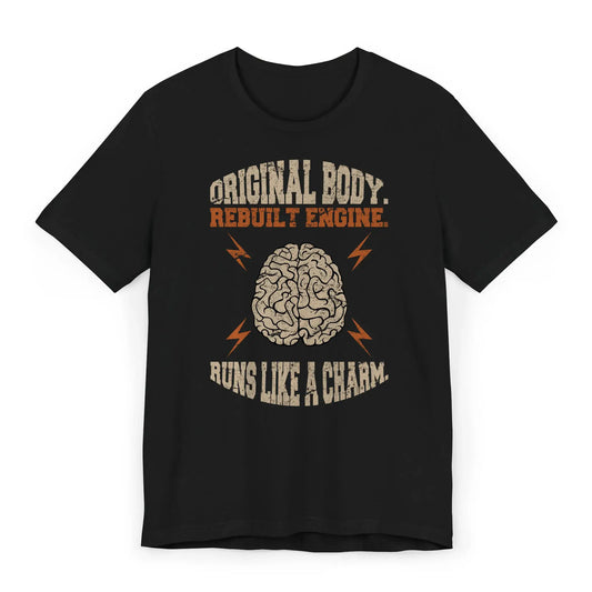 Flat lay of brain surgery recovery shirt with quote “Original Body. Rebuilt Engine. Runs Like a Charm.”